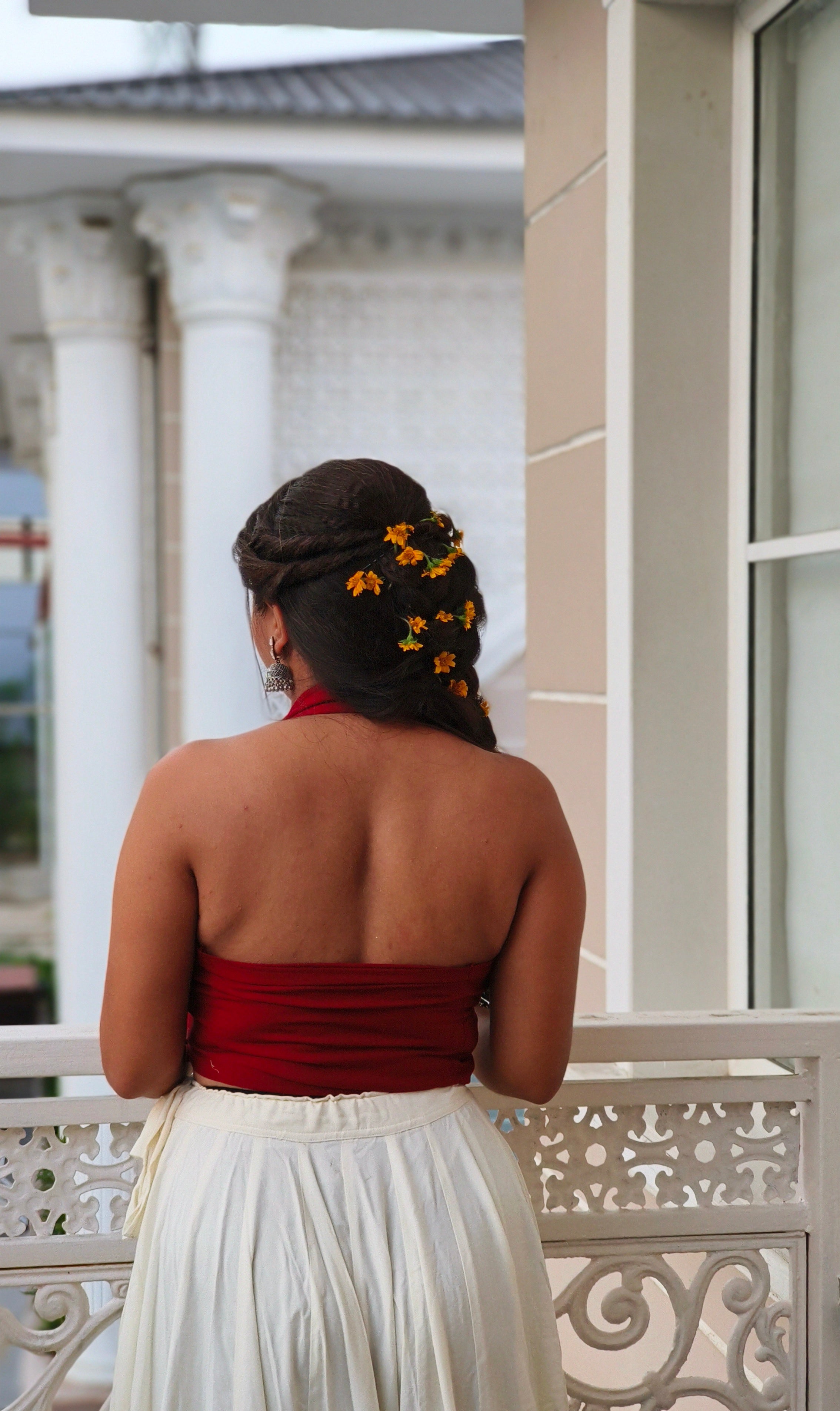 Woman in a red top and white skirt standing on a balcony with columns in the background