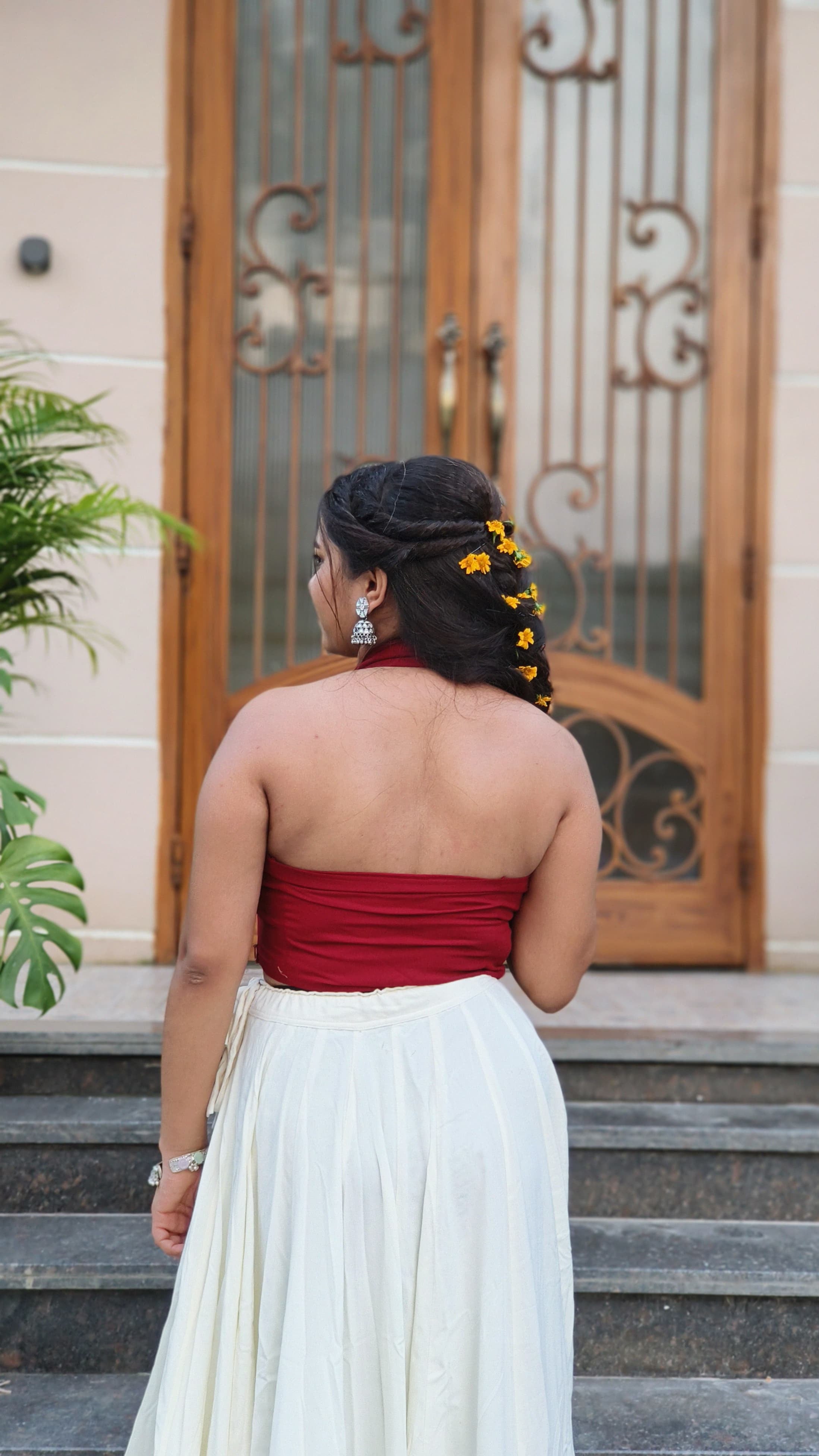 Woman in a red top and white skirt standing on steps with a decorative door in the background