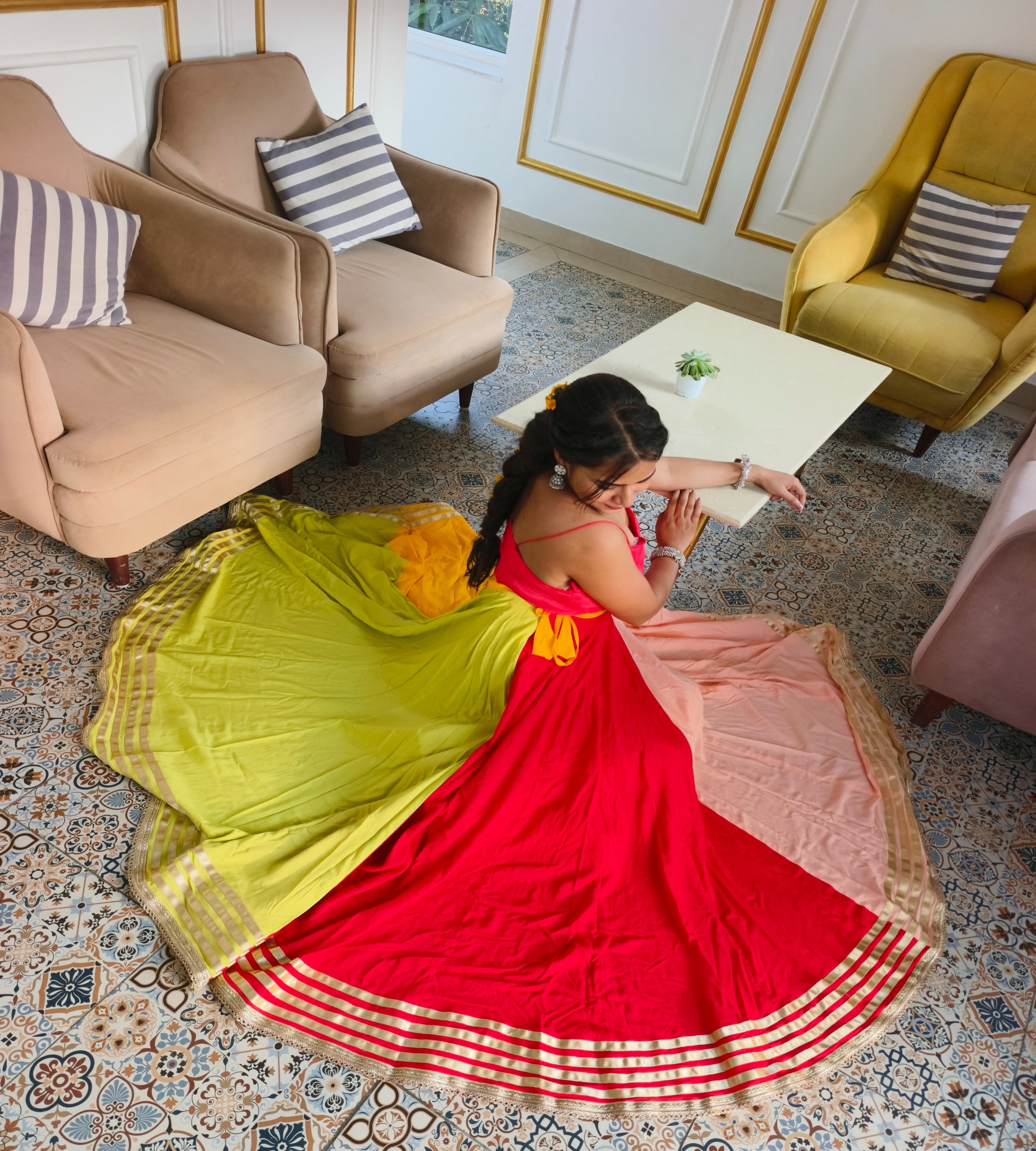 Woman in a colorful saree standing in a stylishly decorated room with furniture and decor.