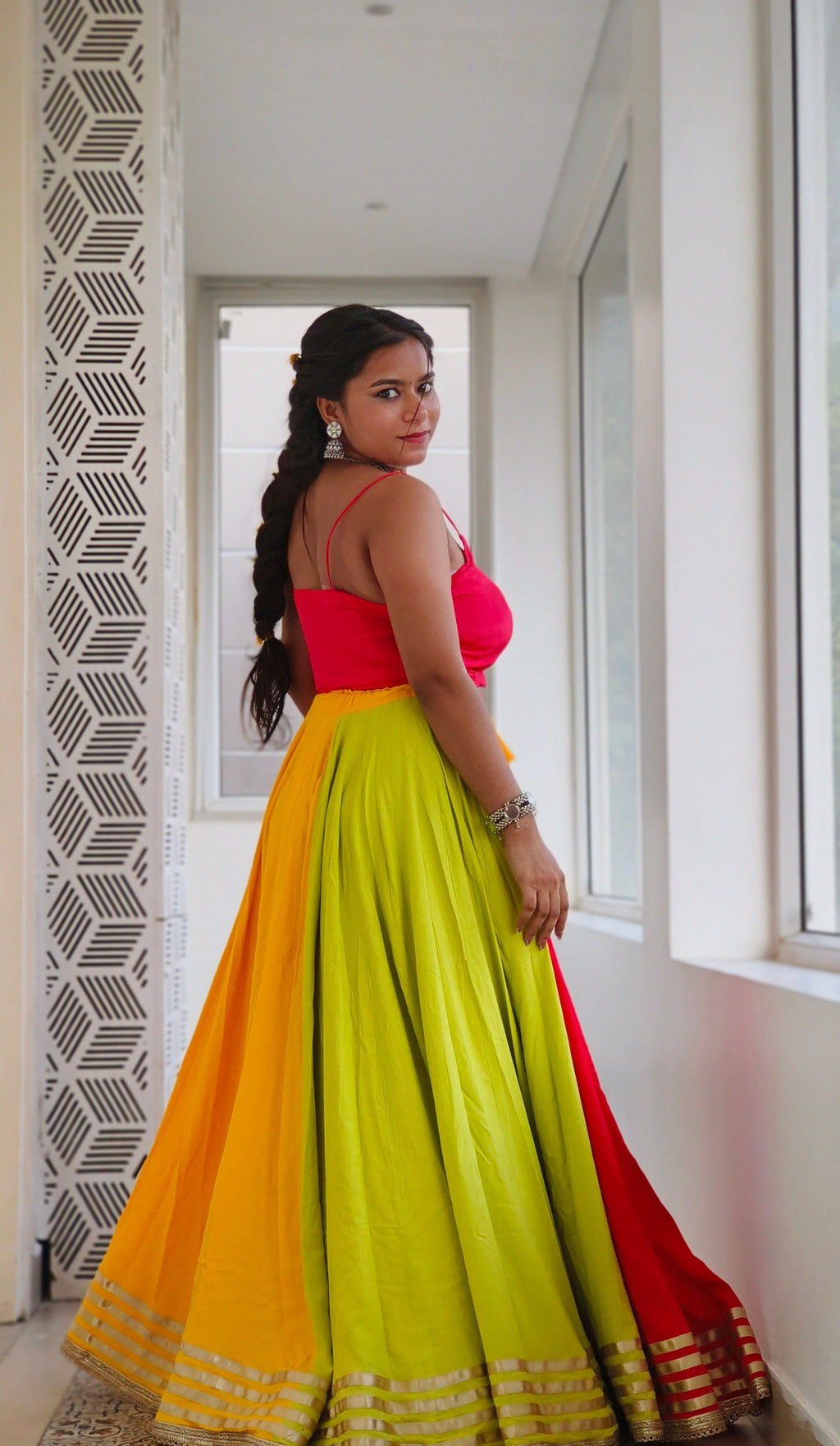 Woman wearing a colorful traditional outfit with a yellow and red skirt in an indoor setting.