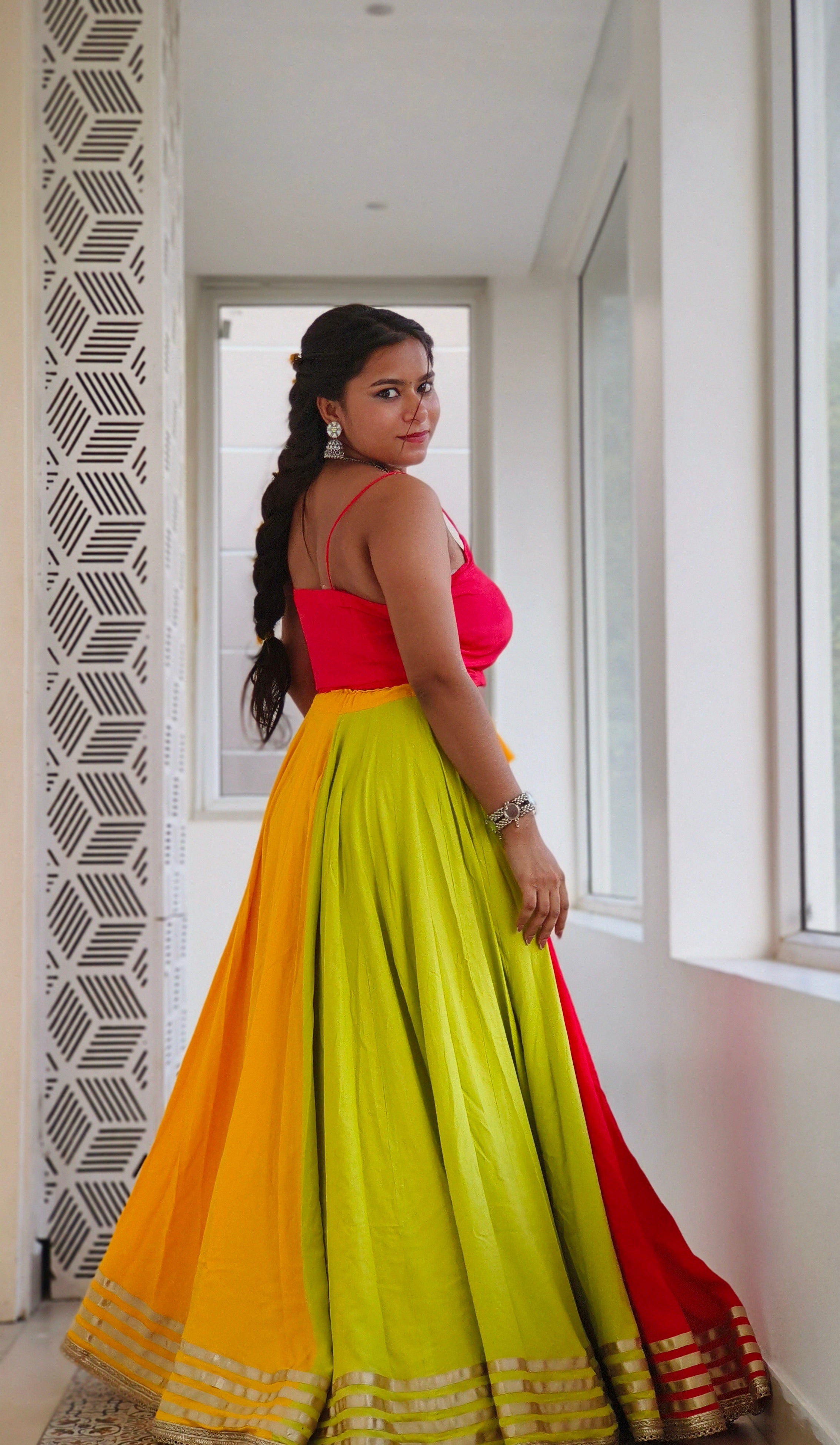 Woman wearing a colorful traditional outfit with a yellow and red skirt in an indoor setting.