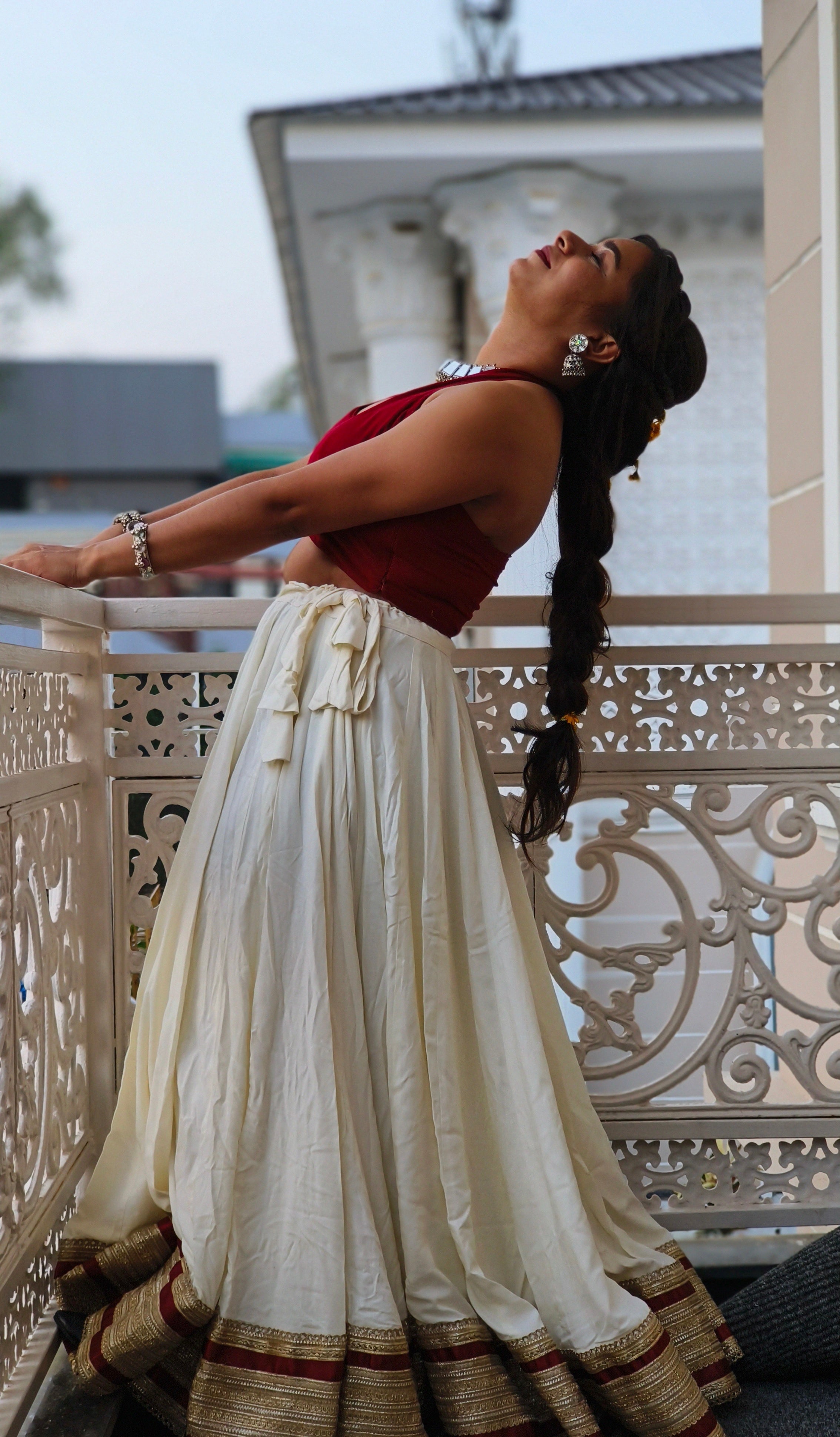 Woman in a white and red traditional outfit standing on a balcony.